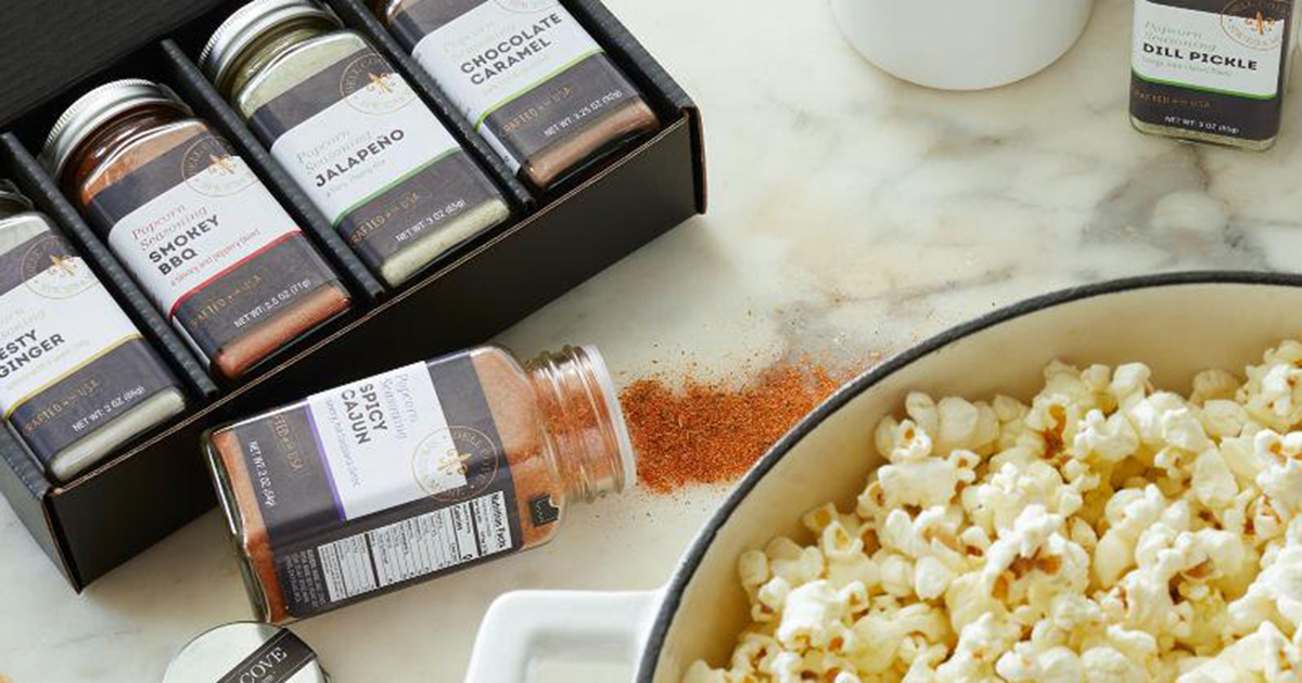 popcorn seasonings in glass containers, next to a bowl full of popcorn kernels